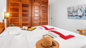 Habitación de hotel con un armario grande de madera, una cama con ropa blanca, un cuadro de veleros y una mesita con cosas para el desayuno.