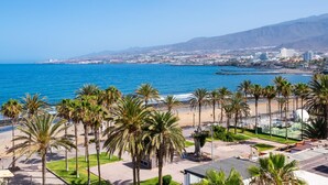 Un paisaje urbano costero con playa, palmeras y cielo azul despejado.