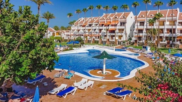 Un resort con piscina central, varios balcones y palmeras.