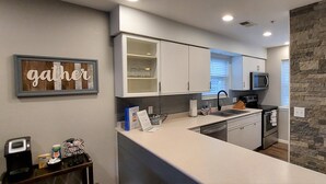 Een moderne keuken met witte kastjes, een ingebouwde magnetron en een accentmuur van steen.