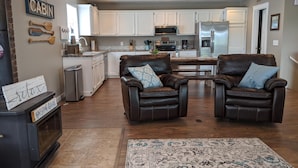 A spacious living room with two leather chairs, a fireplace, and a kitchen in the background.