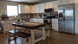 A kitchen with white cabinets, stainless steel appliances, a wooden table, and a window.