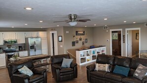 A spacious living room with leather sofas, a coffee table, and a dining area with a white cabinet and a refrigerator.