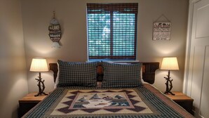 A bedroom with a large bed, two nightstands, a window with blinds, and wall decorations.