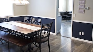 A dining room with a wooden table and chairs, a chandelier, and a wall with a motivational quote.