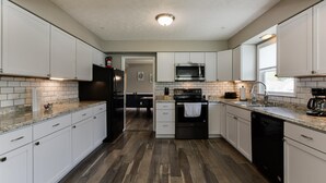 A modern kitchen with white cabinets, a stainless steel refrigerator, a microwave, a stove, and a dishwasher.