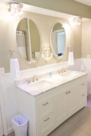 A bathroom with a double sink vanity, two large mirrors, and a trash can.