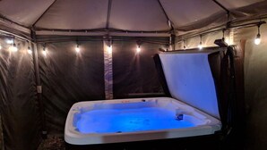 A hot tub inside a tent with a bench in front.
