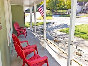 A porch with red chairs, an American flag, and a view of a street with houses.