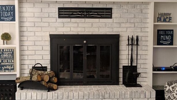 A modern living room with a white brick fireplace, a flat-screen TV mounted above, and motivational wall decor.