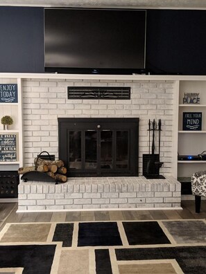 A modern living room with a white brick fireplace, a flat-screen TV mounted above, and motivational wall decor. - Landing Point (Branson)