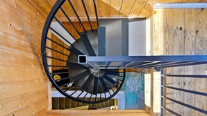 A spiral staircase with a metal handrail and wooden walls, leading to an upper level. - Wonderful Coastal Retreat, Open Layout, Steps Away From Beach, Fireplace, BBQ, Ocean Views (Depoe Bay)
