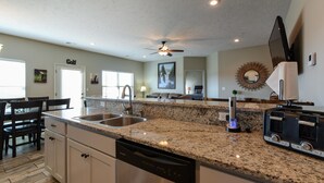 A modern kitchen with granite countertops, stainless steel appliances, and a dining area with wooden chairs. - The Plush (Branson West)