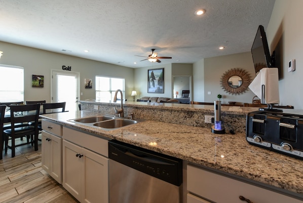 A modern kitchen with granite countertops, stainless steel appliances, and a dining area with wooden chairs.
