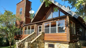 A rustic log cabin with a stone staircase leading to a wooden deck. - Hunters Hike (Yellville)