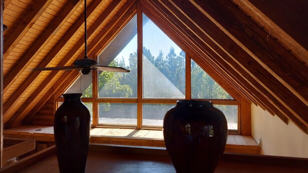 A room with a sloped wooden ceiling, large windows, and two vases on the floor. - Hunters Hike (Yellville)