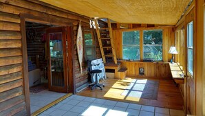 A log cabin interior with a wooden desk, a chair, a ladder, and a large window. - Hunters Hike (Yellville)