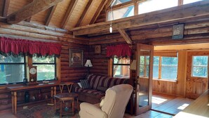 A log cabin interior with a wooden ceiling, a sofa, a chair, a table, and a rug. - Hunters Hike (Yellville)