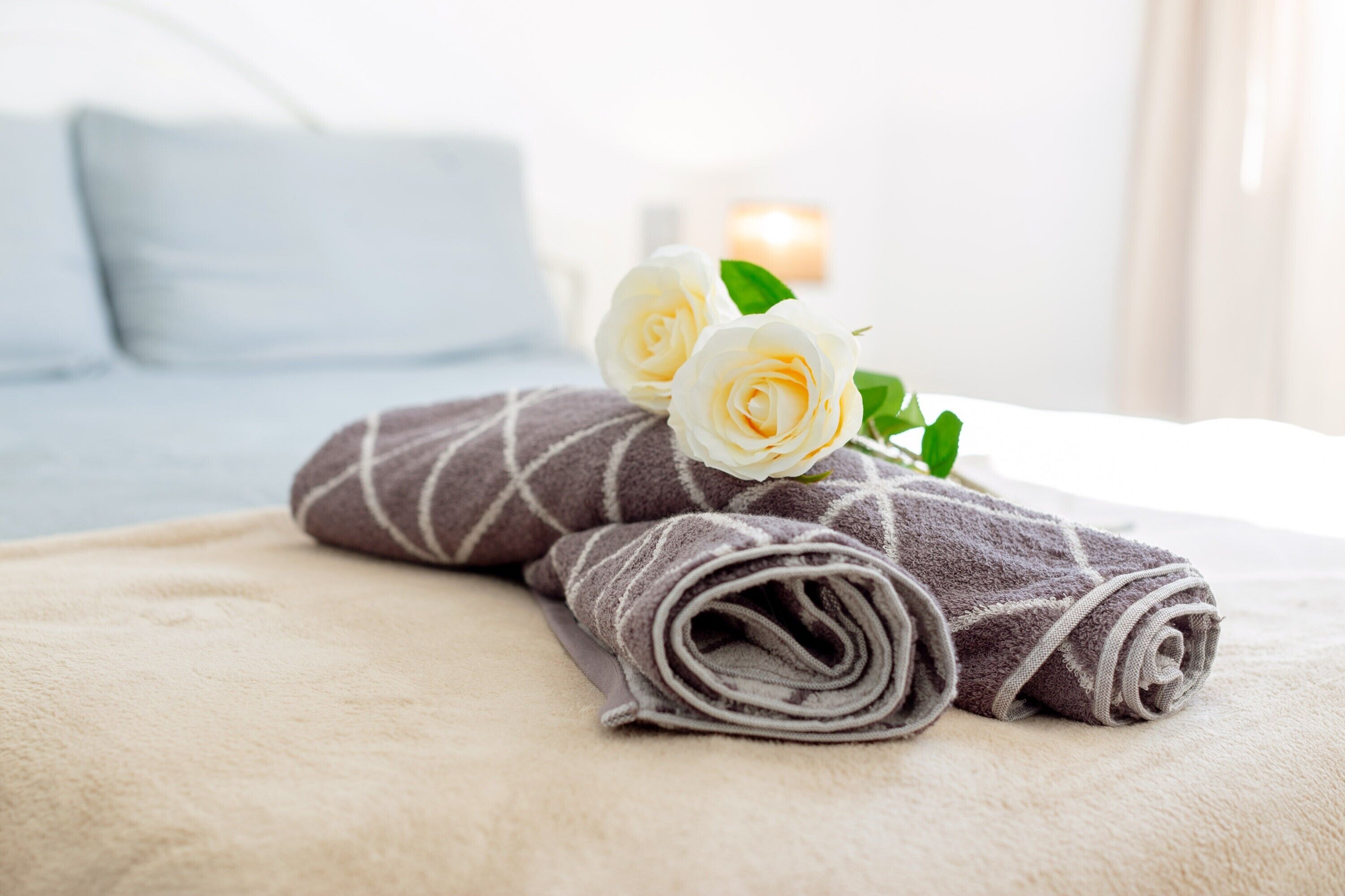 Ein ordentlich bezogenes Bett mit aufgerollten Handtüchern und einer weißen Rose.