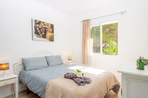 A bedroom with a bed, a bedside table, a lamp, a window with curtains, and a painting on the wall.