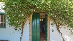 A rustic building with a green door, a wooden bench, and a sign indicating a rural area.