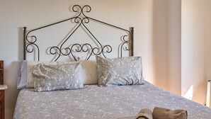 A bed with a patterned bedspread, two pillows, and a rolled towel on the side.
