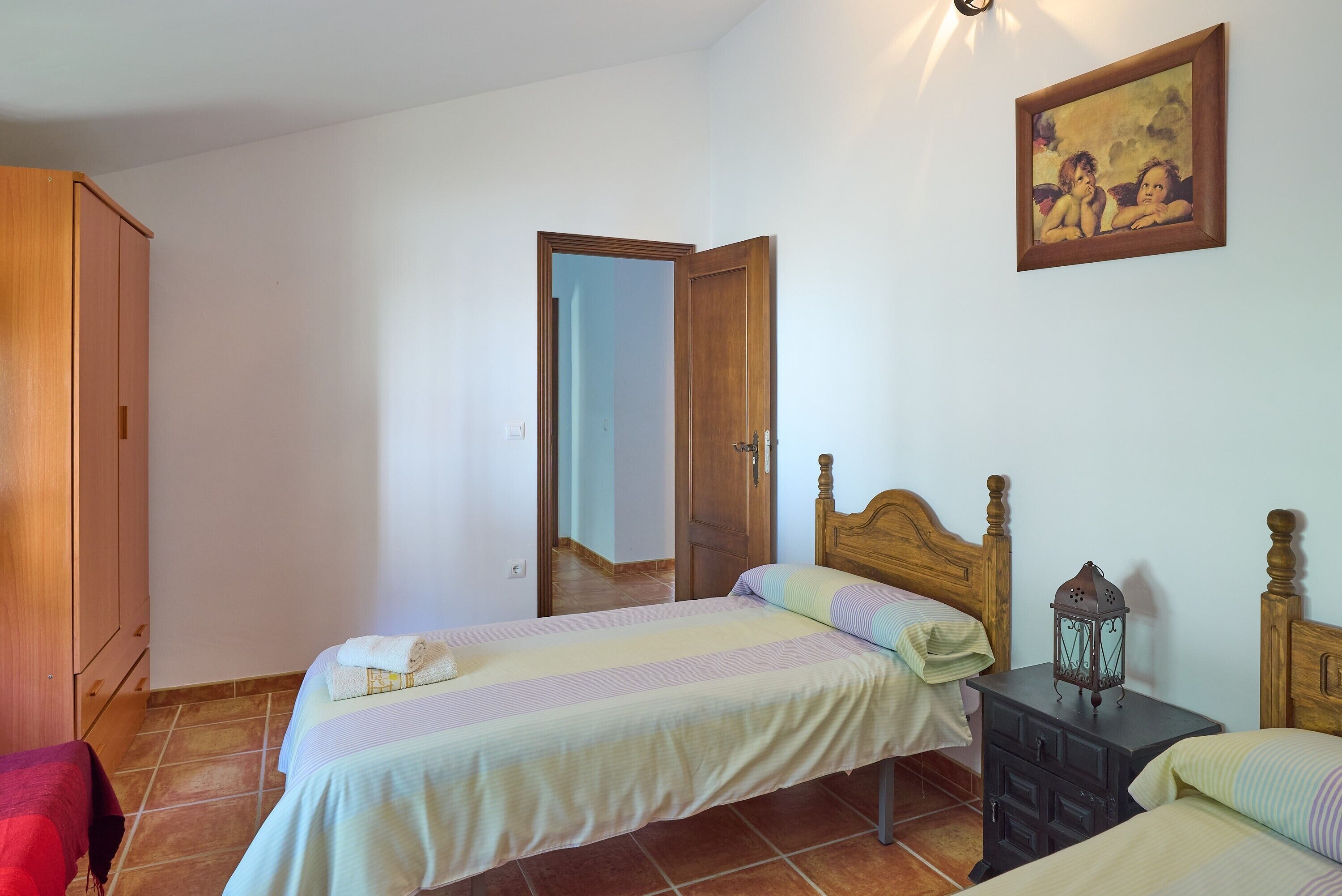 Une chambre avec deux lits, une armoire en bois, une table de chevet avec une lanterne et un tableau au mur.