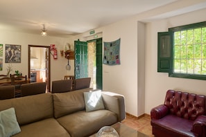 A living room with a sofa, a red leather couch, a dining area with chairs and a table, and a kitchen in the background.