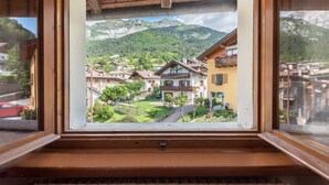 Vista desde una ventana de un pueblo de montaña con edificios tradicionales, cielo despejado y una montaña al fondo.