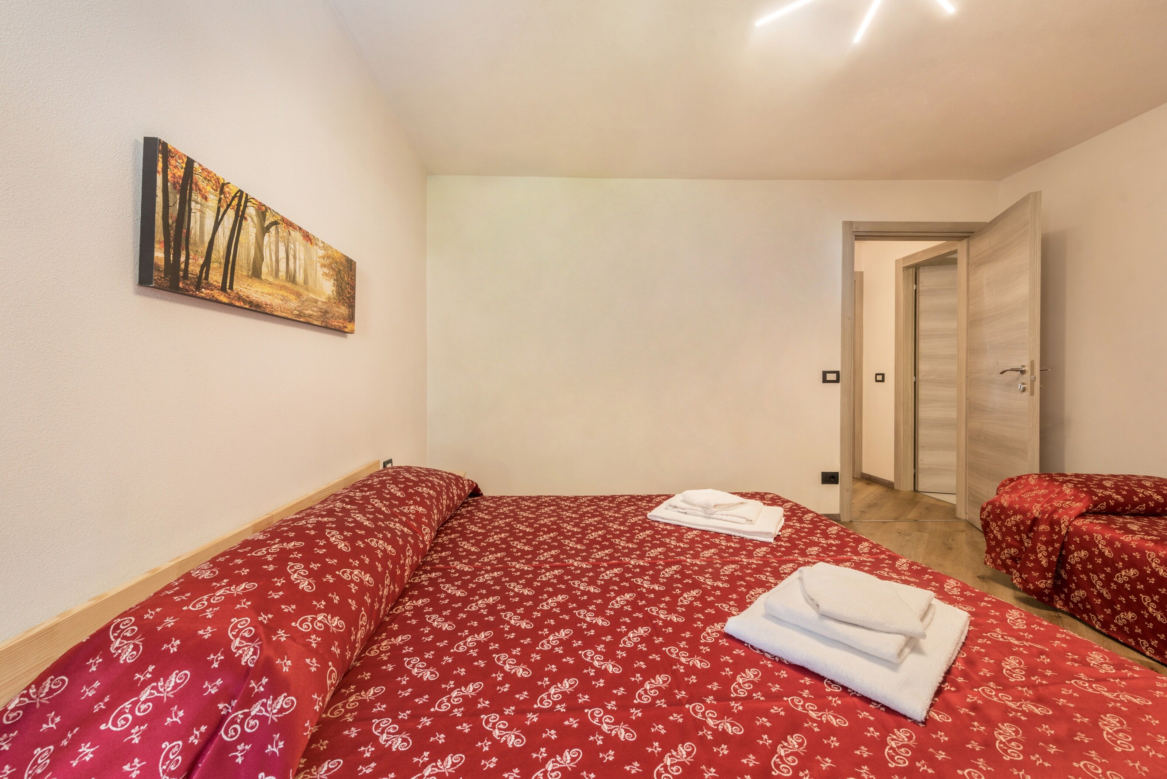 A bedroom with a bed, a painting, and a door leading to another room.
