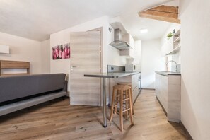 Une cuisine de taille réduite avec un plancher en bois, un canapé gris et un tabouret en bois.