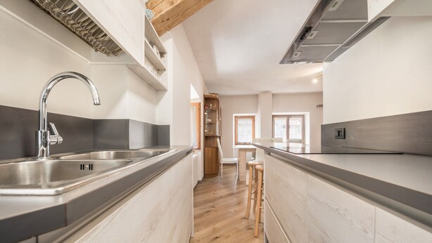Una cocina moderna con un lavamanos de acero inoxidable, suelo de madera y una isla integrada con taburetes.