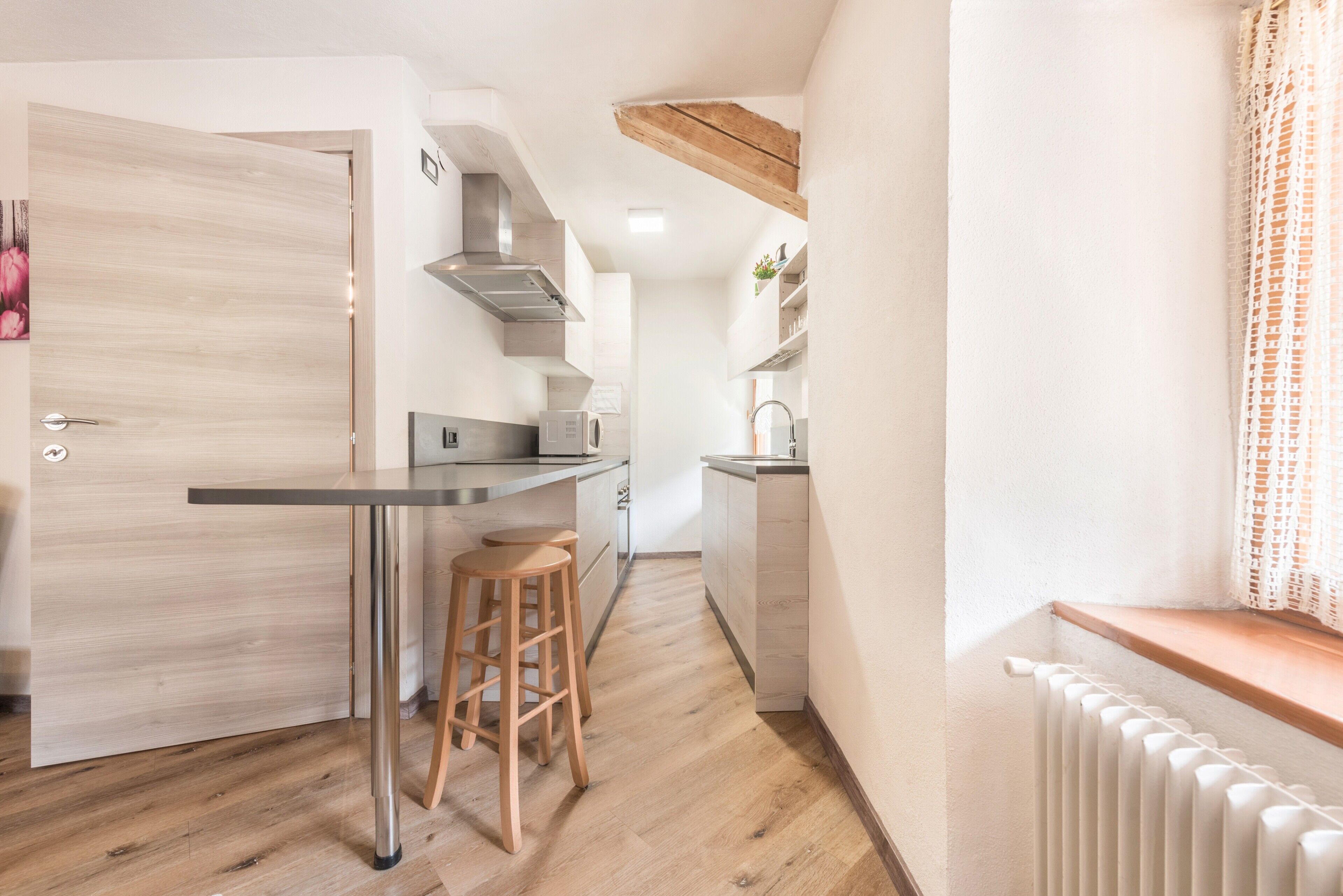 Cocina compacta con suelo de madera, estufa empotrada y un pequeño comedor con taburetes.