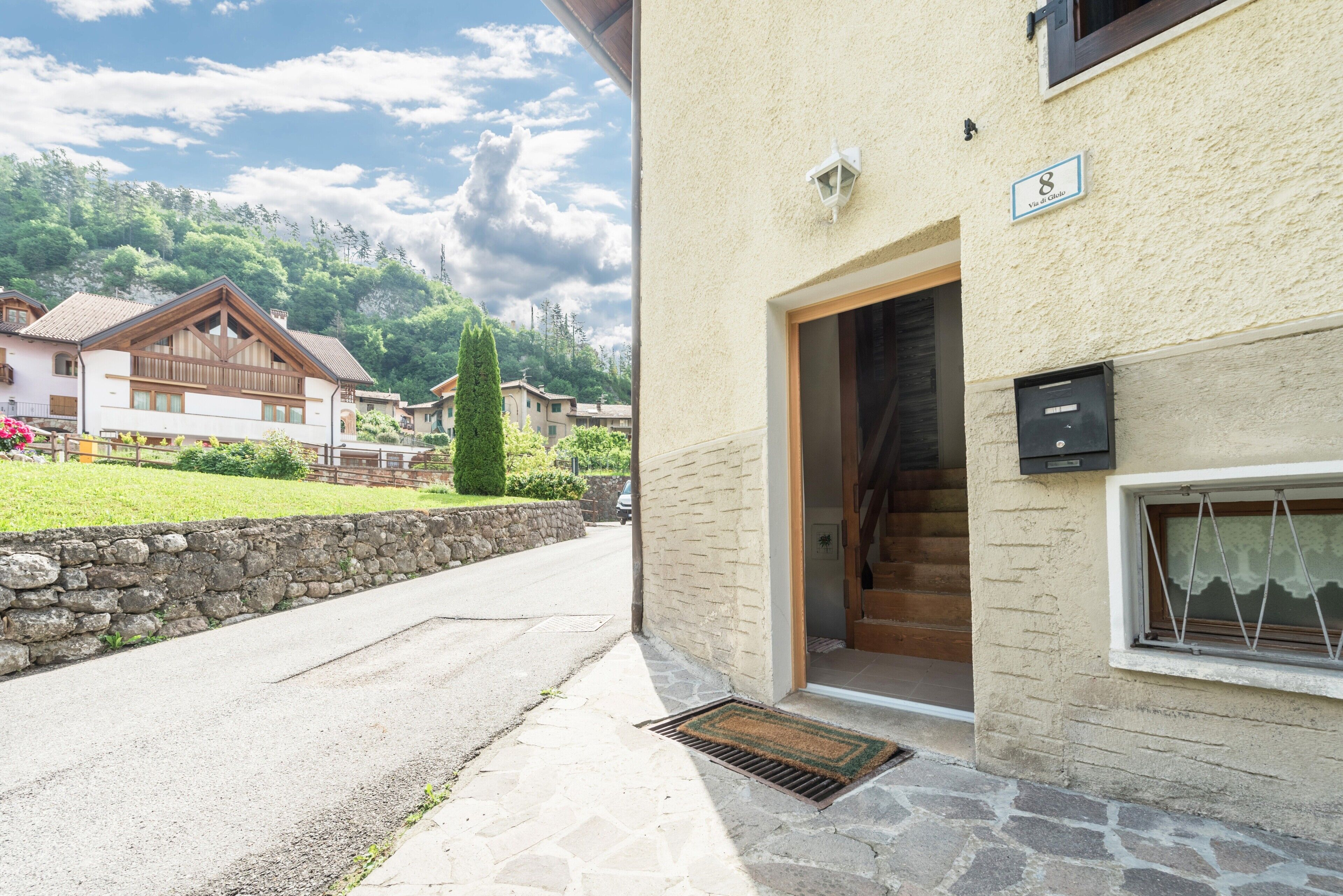 A building with a stone wall, a wooden staircase, and a door leading to a room.