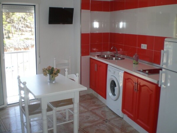 Une cuisine avec des carreaux rouges et blancs, un lave-linge, un évier et une table avec des chaises.