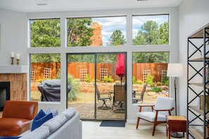 A living room with a fireplace, a sofa, and a view of a backyard with a patio and outdoor seating. - WEST SEDONA RETREAT w/ VIEWS of Coffee Pot Rock! (Sedona)
