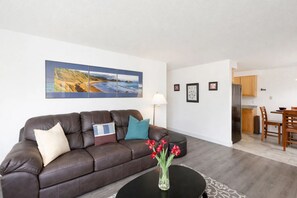 A living room with a brown leather sofa, a black coffee table with a vase of red flowers, and a large landscape painting above the sofa.
