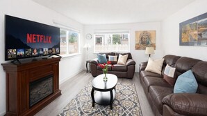 Una sala de estar con chimenea, un televisor mostrando Netflix, un sofá de cuero marrón, una mesa de centro y una alfombra estampada.