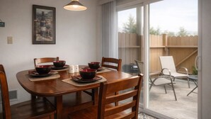 Un comedor con una mesa de madera, seis sillas y cuencos rojos. Se ve una ventana que da a una valla de madera y sillas en el exterior.
