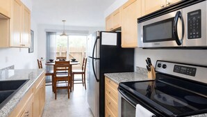 Una cocina moderna con encimeras de granito, armarios de madera, horno empotrado, microondas y refrigerador.