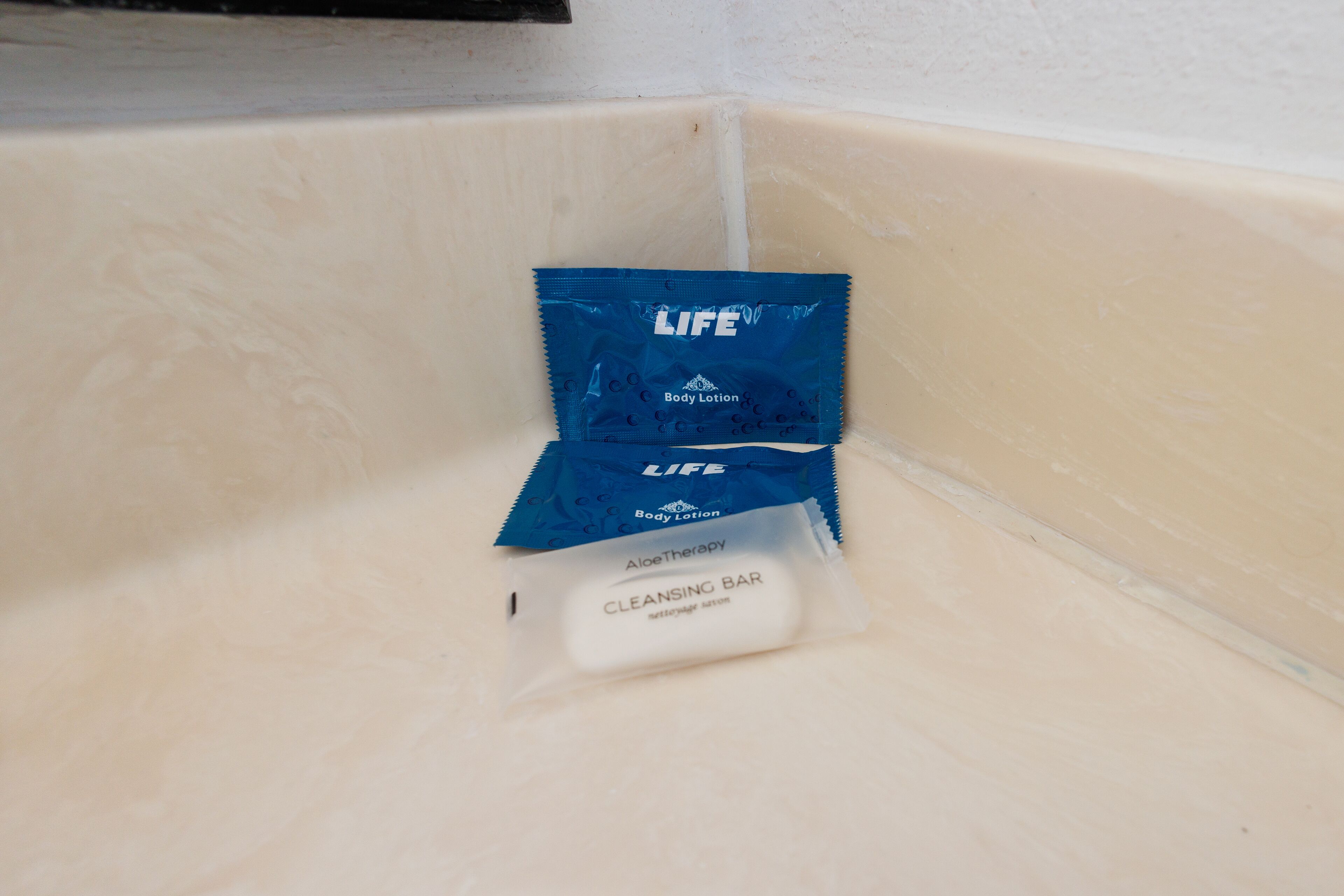 Un flacon de lotion pour le corps de la marque LIFE, de couleur bleue, posé dans un coin de la salle de bain.