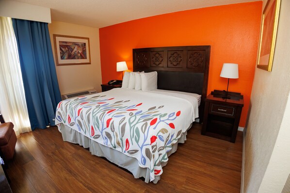 Habitación de hotel con una cama grande, dos mesitas de noche, una butaca y un cuadro en la pared.