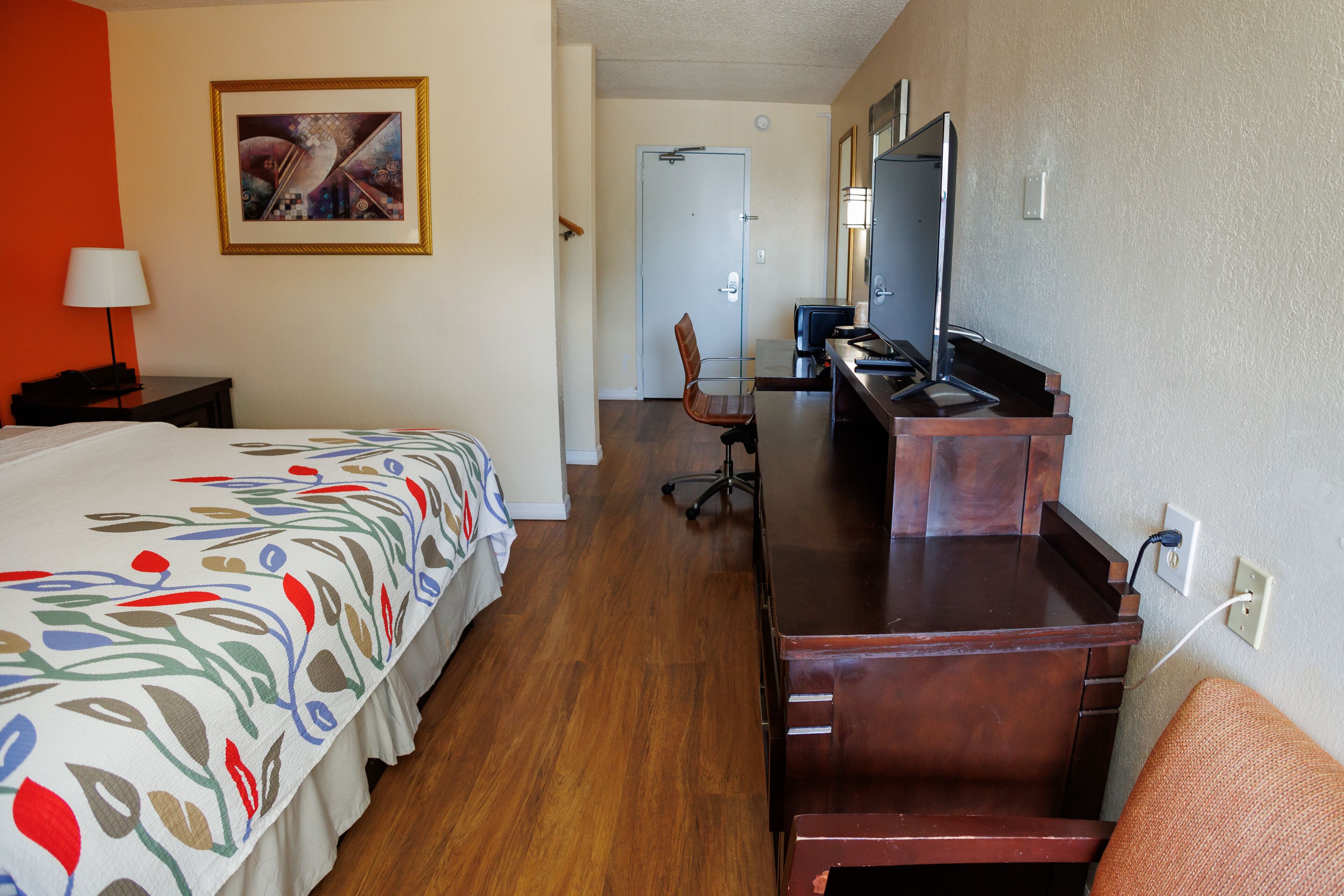 Habitación de hotel con cama, escritorio, silla, televisor y puerta que da a otra habitación.