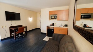 A compact living space with a sofa, a dining table, a TV, and a kitchenette. - Garnet Inn & Suites, Orlando (Orlando)