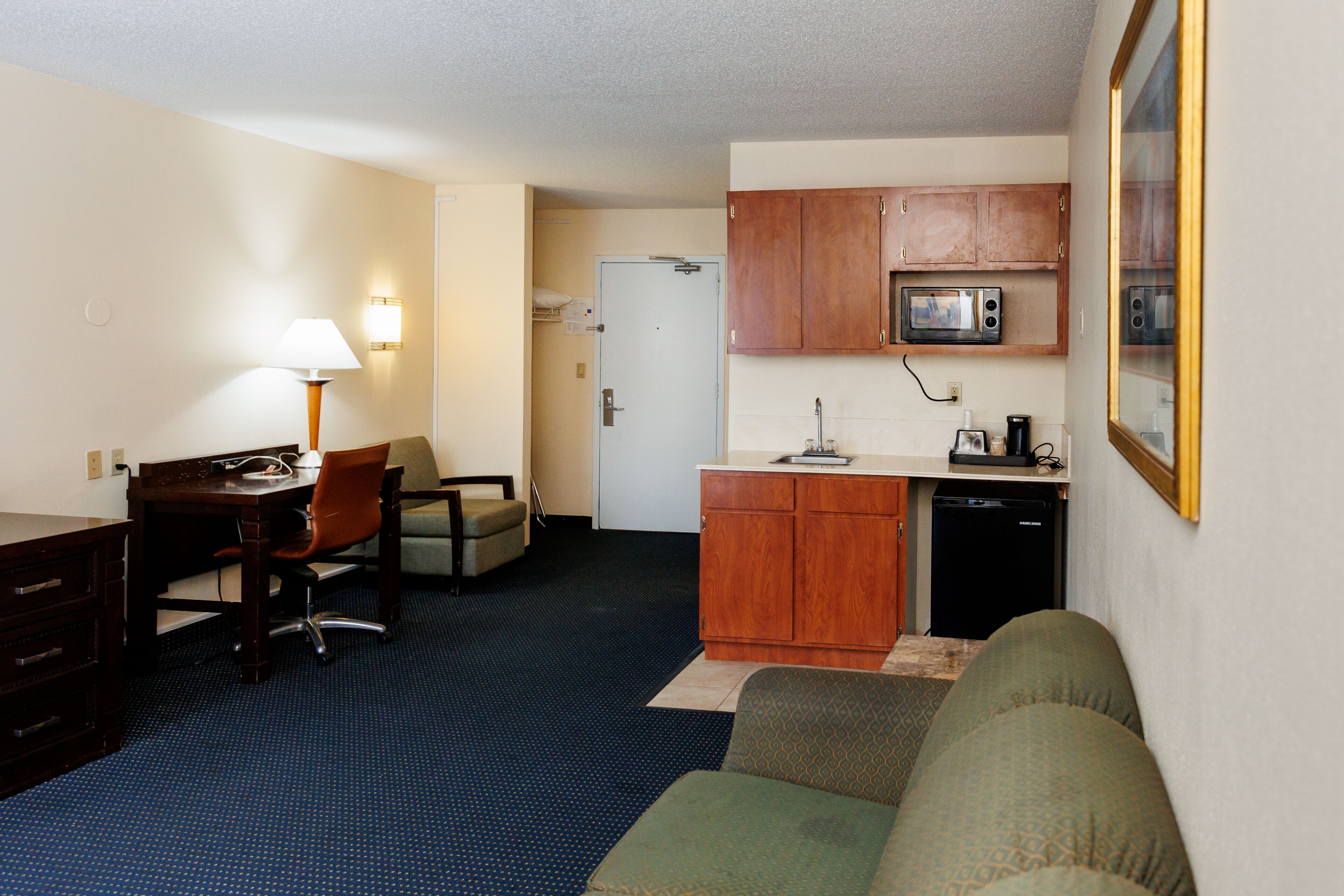 Habitación de hotel compacta con kitchenette, comedor con mesa y sillas, sofá y lámpara.
