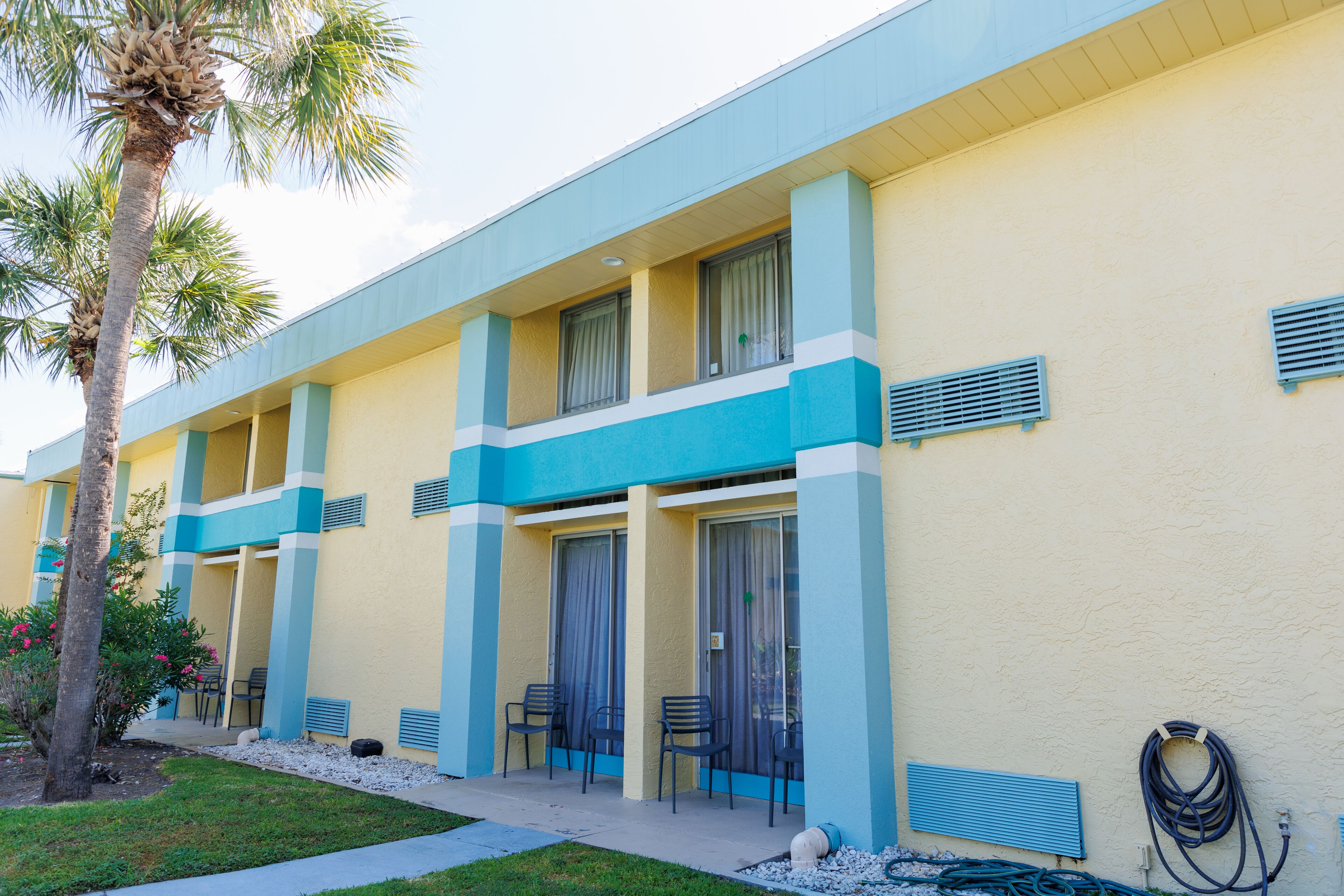 A hotel with a yellow facade, blue accents, and a palm tree in the foreground.