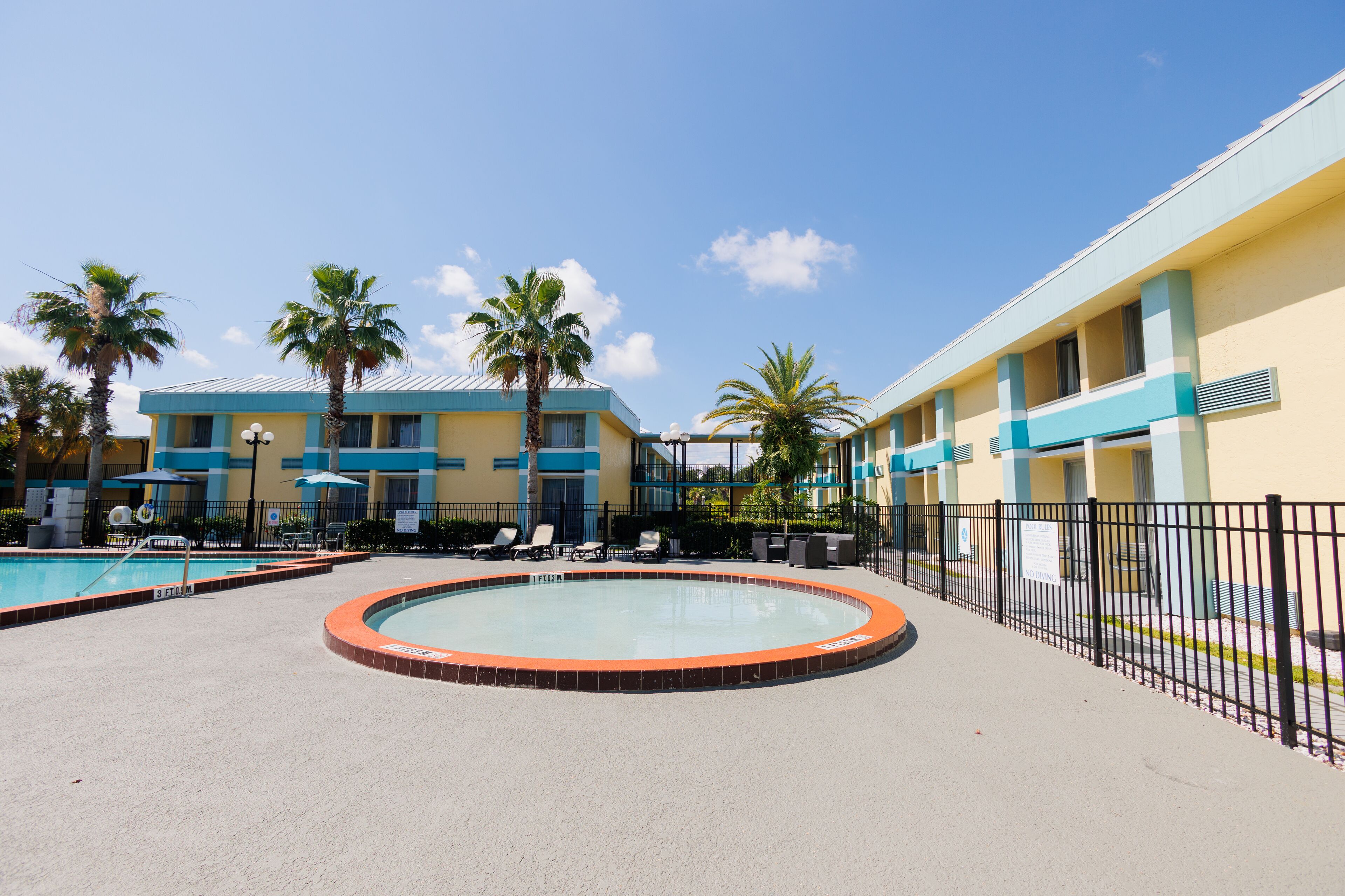A pool area with lounge chairs and a building with blue and yellow exterior walls.