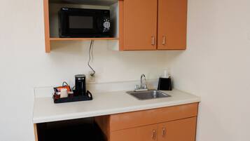 A compact kitchenette with a microwave, coffee maker, and sink.