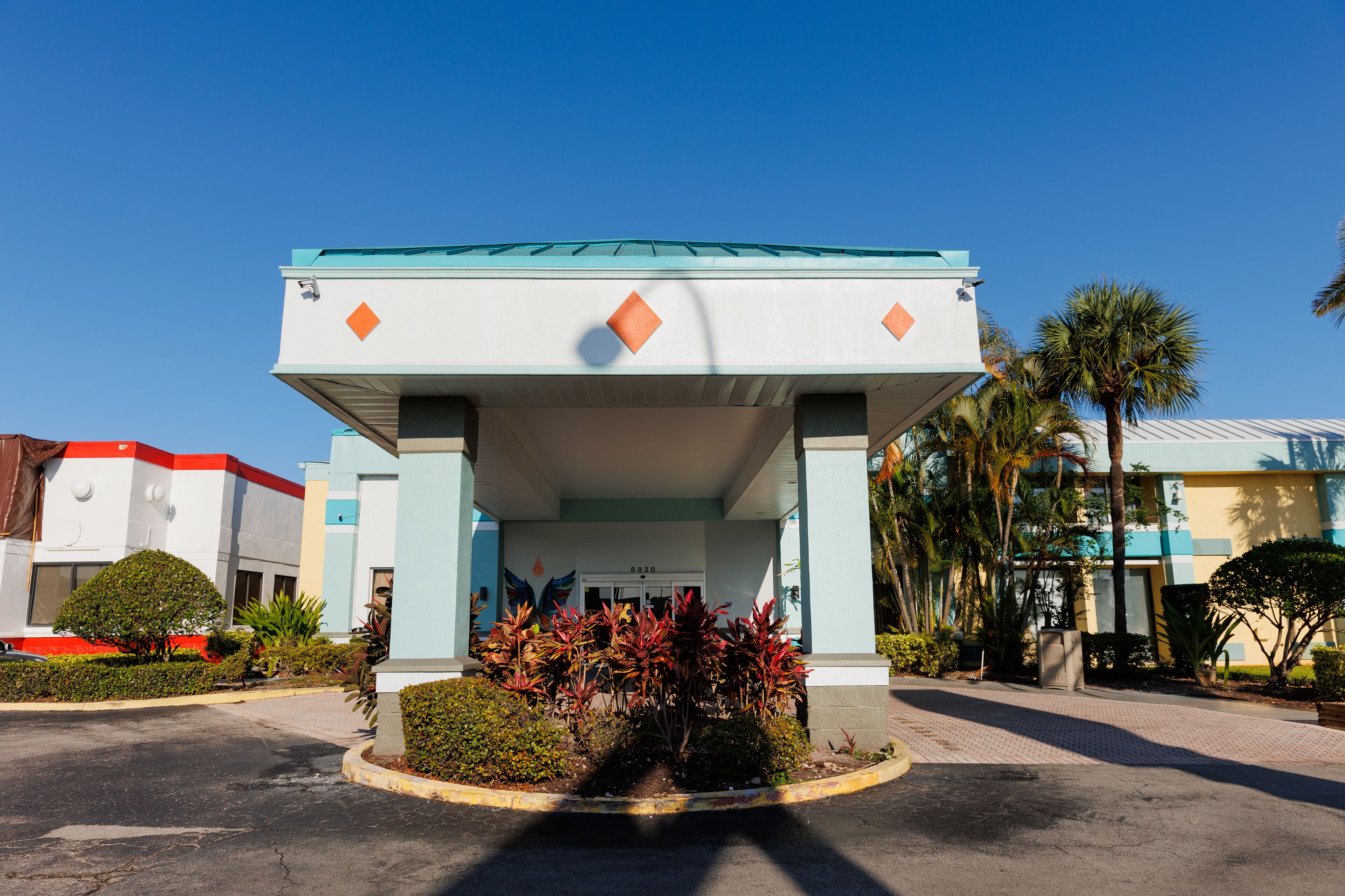 A building with a covered entrance, palm trees, and a clear blue sky.