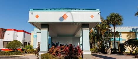 A building with a covered entrance, palm trees, and a clear blue sky.